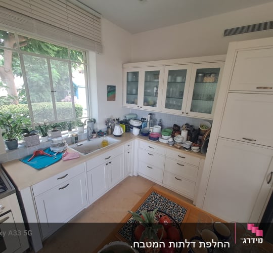 מטבח עם ארונות לבנים, כיור וכלים על השיש